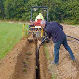 Engineers laying ground source heat pump pipe in a trench