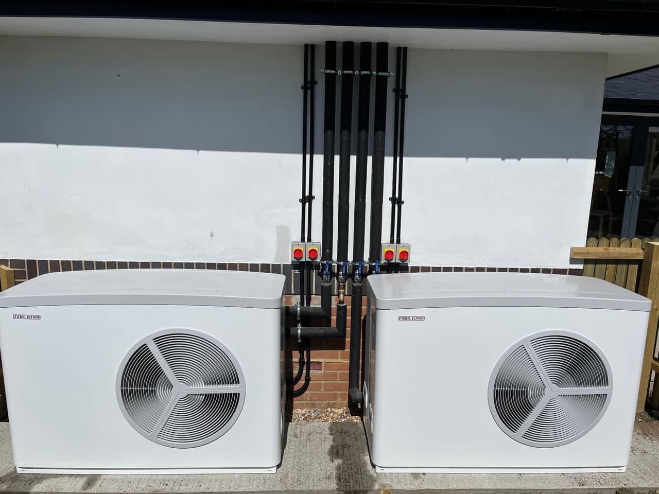 Two air source heat pumps installed by Solwat on a concrete base outside a home